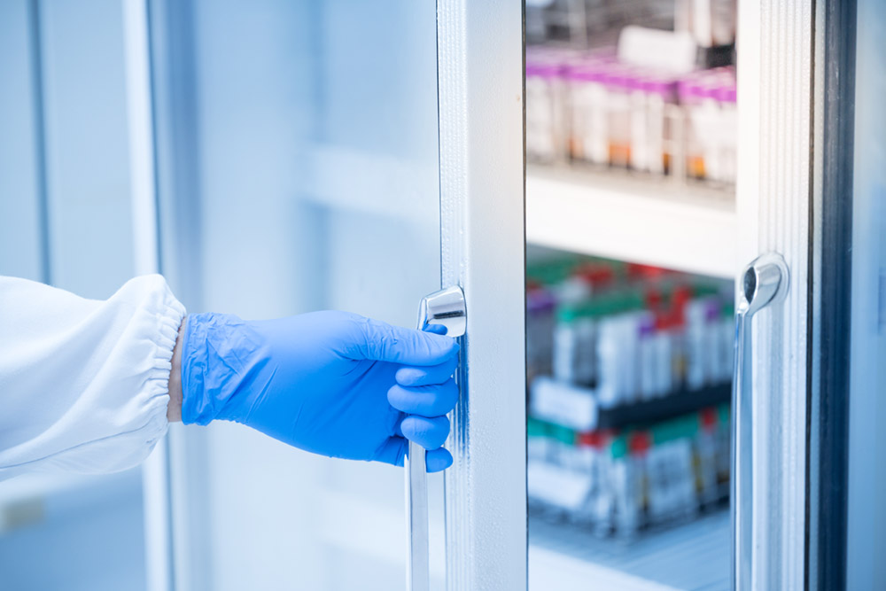 Gloved hand opening laboratory refrigerator containing temperature-sensitive medical vials, emphasizing proper storage conditions for injectable thrombolytic drugs.
